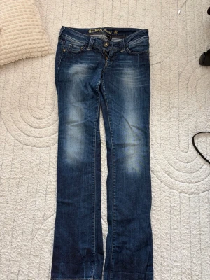 Mörkblå straight jeans från Guess - Snygga mörkblå straight jeans från Guess med slitningar och ljusa partier på låren och knäna. 