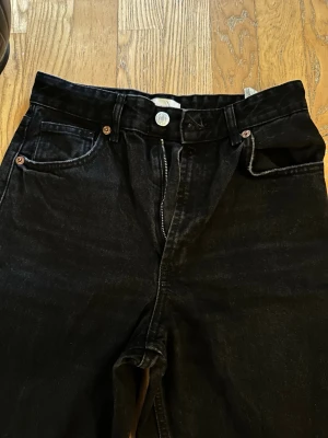 Svarta raka jeans från Zara - Säljer ett par svarta jeans från Zara i rak modell med hög midja. Klassisk femficksdesign och dragkedja med knapp. Jeansen är tillverkade i ett mjukt denimtyg som ger en snygg och avslappnad look. Passsr 36 också