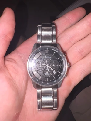 Citizen herrklocka i silver - Stilren herrklocka från Citizen med svart urtavla och detaljerade visare. Klockan har en robust länk i silverfärgat metall och flera små urtavlor för extra funktioner. Perfekt accessoar för dig som gillar klassisk och sportig stil.