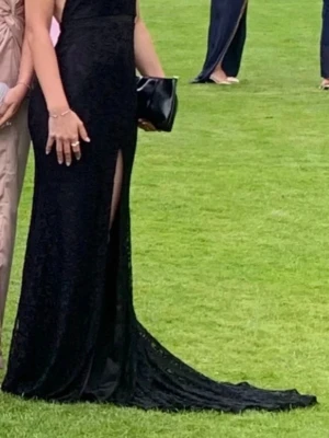 Svart långklänning med slits - Elegant svart långklänning med slits framtill och släp. Klänningen har en figurnära passform och är ärmlös med en axelbandslös design. Materialet ser ut att vara spets eller liknande tyg som ger en lyxig känsla. Långt släp med en diskret ögla som gör det lätt att hålla uppe släppet på klänningen. Omsydd i midjan, längden och runt bysten. Även insydd bh som går att ta bort. Köpt på Dreamwear bridalhouse i Ljungby. Jag är 173 cm lång, kvitto finns på den, 4500kr nypris. 
