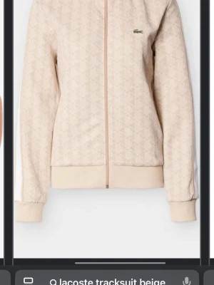 Beige tracksuit från Lacoste - Säljer ett beige tracksuit-set från Lacoste med diskret mönster, dragkedja framtill och vita ränder längs ärmar och ben. Setet har ribbade muddar och den klassiska Lacoste-loggan på bröstet och byxan. Perfekt för chill dagar hemma eller när du vill vara bekväm men ändå snygg den är helt ny aldrig använd säljer då den var för liten för mig köpt för 2699 kvitto finns ej kvar men lapparna är kvar