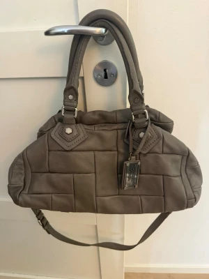 Marc Jacobs väska classic q - Super fin grå Marc Jacobs classic q väska med en unikquiltade design samt silver detaljer! Modellen är classic q, inte den minsta men tror detta är mellan. Inuti finns 2 mindre fack och ett större med dragkedja Tyvärr har några sömmar lossnat vid dragkedjan men skulle inte påstå att det stör användningen samt att det går lätt att sy igen! Finns även småsmå fläckar på väskan men det är verkligen super små så inget man lägger märke till 🥰