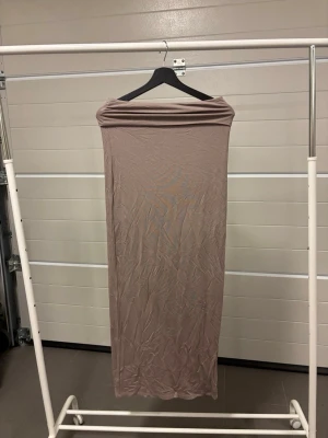 Beige långkjol från Gina Tricot - Säljer en beige långkjol från Gina Tricot i mjukt och stretchigt syntetmaterial. Kjolen har rak passform och bred linning upptill, perfekt för en clean och enkel look.