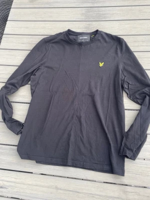 Svart långärmad topp från Lyle & Scott - Säljer en svart långärmad topp från Lyle & Scott med rund hals och den klassiska gula logon broderad på bröstet. Tillverkad i mjuk bomull som känns skön mot huden. Enkel och stilren design som passar till det mesta. Den är oanvänd. Hör av dig vid frågor. Billigare pris vid snabb affär!