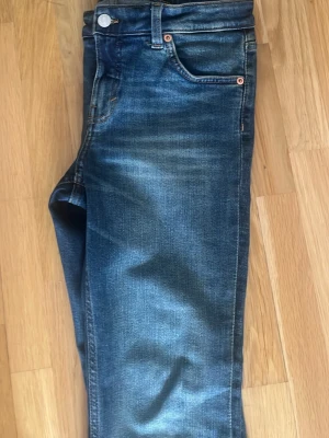Blå jeans från Monki med normal passform - Säljer ett par klassiska blå jeans från Monki med bootcut stil. Stretchiga i tyget så storleken är inte helt fasst spikad. Uppsydda i benen så skulle passa någon som är 1.60-1.62 i längd. Helt oanvända. Ingen prislapp