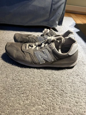 Grå New Balance sneakers - Snygga grå sneakers från New Balance med klassisk N-logga på sidan. Skorna har mesh- och mockadetaljer, vita skosnören och vit/grå sula. Perfekta för dig som gillar en stilren och sportig look. Ingen box
