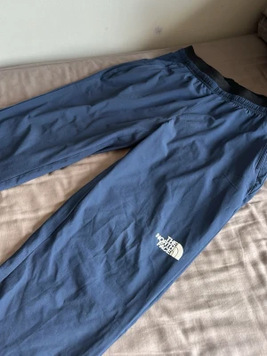 Blå mjukisbyxor från The North Face - Snygga blå mjukisbyxor från The North Face med resår i midjan och diskret logga på benet. Tillverkade i mjukt material som känns skönt mot huden. Perfekta för chill dagar eller när du vill ha det bekvämt. Kan diskutera pris vid snabbaffär