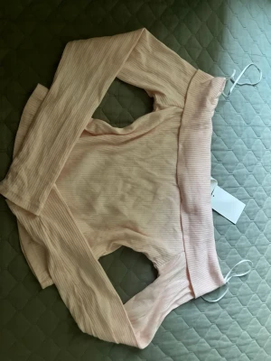 Ljusrosa ribbad offshoulder topp - Trendig ljusrosa offshoulder topp med långa ärmar och ribbad struktur. Toppen har en bred kant upptill som ger en snygg passform och är perfekt för dig som gillar en stilren men ändå söt look. Materialet känns mjukt och stretchigt.