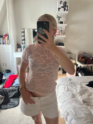 Ljusrosa spetsblus med blommönster - Säljer en ljusrosa, kortärmad spetsblus med blommigt mönster. Toppen är lätt transparent och har en rund halsringning. Perfekt för dig som vill ha en feminin och trendig look.
