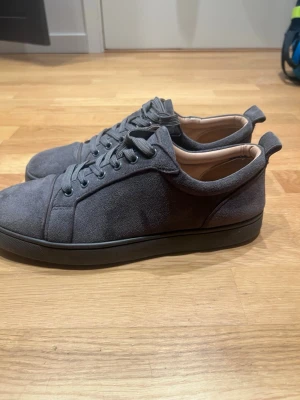 Loubs - Snygga mörkgrå sneakers i mocka med lågt skaft och matchande grå skosnören. Skorna har en stilren design med svarta sulor och diskreta sömmar. Insidan är ljusbeige och de har en klassisk snörning framtill. Perfekta för en clean och modern look.