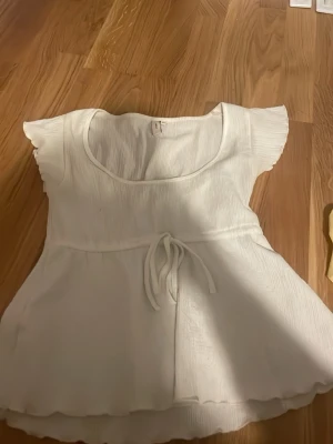 Vit blus med knyt och volang - Söt vit blus med korta ärmar, rund halsringning och knyt i midjan. använd fåtal gånger. 