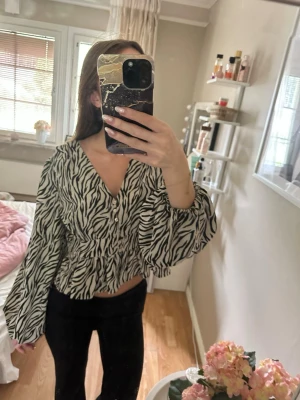 Zebramönstrad blus med v-ringning - Säljer en snygg zebramönstrad blus med v-ringning och ballongärmar. Blusen har resår i midjan för en smickrande passform och är i ett lätt, luftigt material. Perfekt för dig som vill sticka ut med ett trendigt mönster.