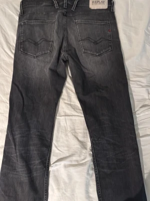 Svarta raka jeans från Replay - Säljer ett par svarta Anbass jeans från Replay med raka ben och klassisk femficksdesign. Jeansen har snygga slitningar och kontrastsömmar, samt Replay-logga på bakfickan. Perfekta för en avslappnad och trendig look. Storlek: W33 L34
