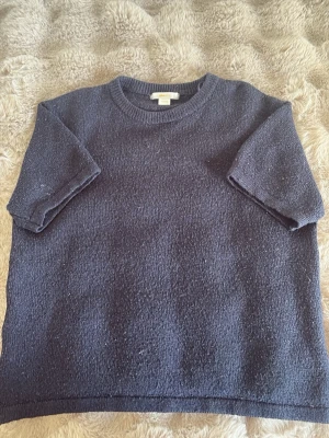 Mörkblå stickad t-shirt - En enkel och stilren mörkblå stickad t-shirt med korta ärmar och rund halsringning. Tröjan har en rak passform och är gjord i ett mjukt stickat material som känns skönt mot huden. Perfekt för dig som gillar minimalistisk stil.