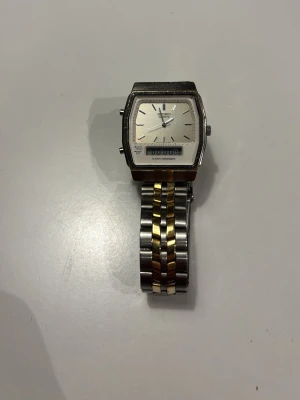 Seiko herrklocka i silver och guld - Klassisk Seiko herrklocka med rektangulär urtavla i silver och länkarmband i både silver och guld. Urtavlan har tydliga markeringar och digital display. Armbandet är i metall och har en smidig låsmekanism.