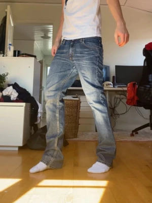 Blå baggy jeans med slitningar - Säljer ett par blå baggy jeans med tydliga slitningar och ljusa tvättade partier. Jeansen har raka ben, klassiska fem fickor och kontrastsömmar. Perfekta för en avslappnad och trendig stil.
