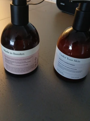 Under Your Skin balsam och tvål - Två bruna plastflaskor med pump, en med etiketten 'Under Your Skin Density Conditioner' och en med 'Made in Sweden'. Balsamet är för ökad hårtäthet och volym. Flaskorna har minimalistisk design och rymmer 250 ml.