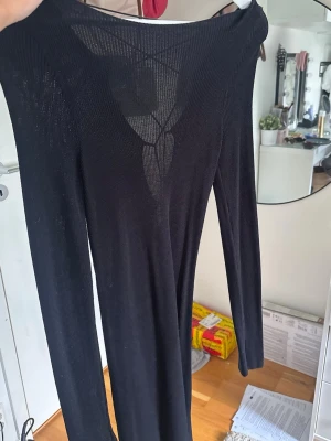 Svart långärmad klänning med snörning - Hanna Schönbergs kollektion från NA-KD. Svart långärmad klänning med snygg snörningsdetalj framtill och v-ringad hals. Klänningen är figurnära och har en enkel, stilren design som passar perfekt till olika tillfällen. Materialet ser ut att vara stretchigt och bekvämt.
