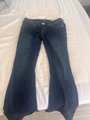 Mörkblå bootcut jeans True Religion - Säljer ett par mörkblå bootcut jeans från True Religion med kontrastsömmar och ikoniska fickdetaljer bak. De är aldrig använda, bara tvättade en gång, Säljer då det är för stora för mig