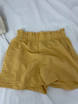 Gula högmidjade shorts Gina Tricot - Säljer ett par ljusgula högmidjade shorts från Gina Tricot i mjuk bomull. Shortsen har resår i midjan och en avslappnad passform, perfekta för varma dagar. Enkla att matcha och superbekväma!