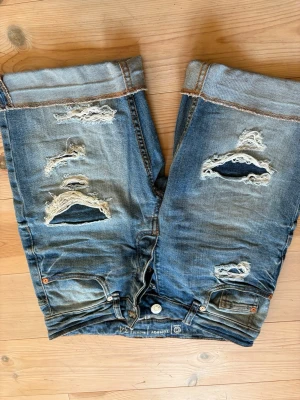 Blå slitna jeansshorts Tomboy - Säljer ett par blå jeansshorts från Tomboy med slitna detaljer och råa kanter. Shortsen har flera revor framtill för en trendig, avslappnad look och klassisk femficksdesign. Perfekta för sommarens alla äventyr!