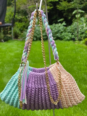 Flerfärgad virkad handväska med kedja - Unik handväska i virkad design med breda ränder i mintgrönt, lila och beige. Väskan har en flätad axelrem i matchande färger och en guldfärgad kedja som detalj. Perfekt för dig som gillar färg och vill sticka ut. Materialet är tjockt garn som ger en mjuk och trendig look.