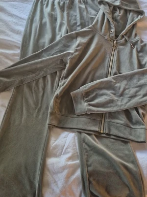 Grått velour loungewear-set - Mysigt loungewear-set i mjuk grön velour. Setet består av en zip-hoodie med huva och dragkedja samt matchande byxor med resår i midjan. Perfekt för chill dagar hemma eller när du vill vara extra bekväm.