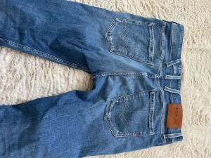 Blå raka jeans från Replay - Säljer ett par blå jeans från Replay med raka ben och slitna detaljer framtill. Jeansen har klassiska fem fickor, ljus tvätt och kontrastsömmar. Perfekta för en avslappnad och trendig look.