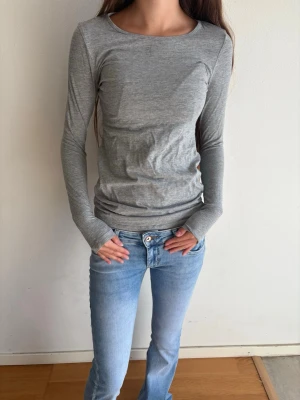 Grå långärmad topp i bomull - En enkel och stilren grå långärmad topp med rund halsringning. Tillverkad i mjuk bomull som sitter skönt mot kroppen. Perfekt att matcha med jeans eller kjol för en clean look.