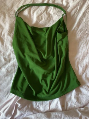 Grönt linne med tunna axelband - Snyggt grönt linne med tunna axelband och draperad framsida. Perfekt för dig som vill ha en enkel men trendig topp till sommaren. Materialet känns mjukt och följsamt, och toppen har en avslappnad passform.