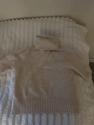 Beige stickad polotröja kort ärm - Mysig beige stickad polotröja med korta ärmar och bred ribbstickad kant vid ärmslut och nederkant. Perfekt till hösten.