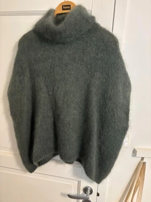 Grå fluffig stickad polotröja - Mysig och oversized stickad polotröja i en mjuk, fluffig grå nyans. Tröjan har hög polokrage och en lös passform som ger en avslappnad look. Perfekt för kalla dagar och enkel att styla med jeans eller kjol.