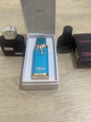3 olika parfymer valtinon bir intens vulckan fue ramza lattafa - Säljer en exklusiv parfym i en snygg turkos flaska med gulddetaljer och dekorativt lock. Flaskan ligger i en elegant vit ask med mönster. Perfekt för dig som vill ha något unikt och stilrent på parfymhyllan.