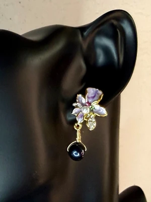 Romantiska Blomörhängen med Emalj, Strass & Svarta Pärlor – Nya - Romantisk Retrostil - Cottagecore - Söta och romantiska blomörhängen med lila emalj, glittrande strass och svarta pärlor. Den gyllene metallen ger en elegant vintageinspirerad känsla. Perfekta till fest, bröllop, student eller när du vill ge din outfit en feminin detalj. Nya och oanvända. Mått: ca 3,5 × 1,7 cm. Material: gyllene metall, emalj, strass och dekorativa pärlor. Jag ger gärna bundelrabatt vid köp av flera varor.