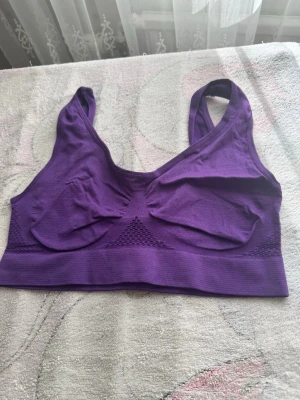 Lila sömlös sport-bh - En lila sport-bh i sömlös design med breda axelband och lätt stöd. Bh:n har ribbade detaljer under bysten och mesh-liknande partier för extra ventilation. Mjuk och stretchig, perfekt för en aktiv vardag.