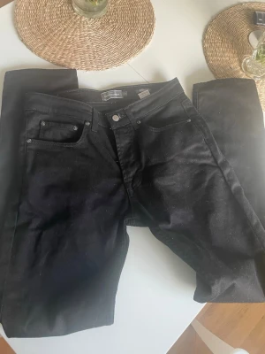 Svarta raka jeans - Säljer ett par svarta jeans med klassisk femficksmodell och raka ben. Jeansen har silverfärgade nitar och knapp, samt bälteshällor i midjan. Materialet är denim med en matt finish. Perfekta för en stilren och enkel look. Dem är använda några fåtal gånger. Hör av dig vid frågor! Kan gå ner i pris vid snabb affär
