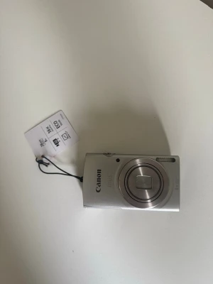 Canon IXUS silver digitalkamera - Snygg och kompakt Canon IXUS digitalkamera i silverfärg med rundade kanter. Kameran har en stor display på baksidan och flera knappar för enkel navigering. Utrustad med 16x optisk zoom och ECO-läge. Perfekt för dig som vill ha en smidig kamera i metall.