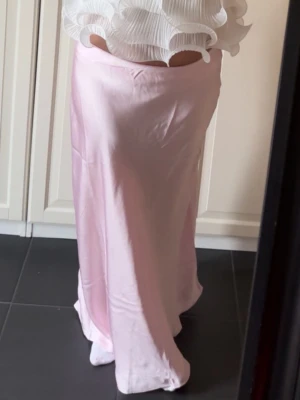 Ljusrosa långkjol i satin - Säljer en elegant ljusrosa långkjol med mjuk glansig satinlook. Endast använd 1 gång💕