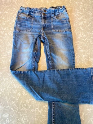 Blå jeans från h&m - Säljer ett par blå jeans med trendig paperbag-midja och dubbla knappar. Jeansen har klassiska fem fickor, bälteshällor och snygga slitningar för en avslappnad look. Tillverkade i mjukt denimtyg som är skönt att bära hela dagen.