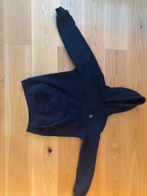 Svart hoodie från HUGO boss - Snygg svart hoodie från HUGO boss med klassisk huva och stor magficka framtill. Diskret HUGO-logga på bröstet. Tillverkad i mjukt material som känns skönt mot huden. Perfekt för en avslappnad och trendig look.