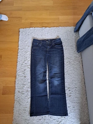 Mörkblå bootcut jeans - Säljer ett par mörkblå bootcut jeans med klassisk femficksdesign och normal passform. Jeansen har en lätt utsvängd benform och är tillverkade i bomull med lite stretch för extra komfort. Perfekta till en avslappnad och trendig look.