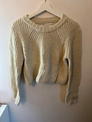 Beige stickad tröja från ONLY - Mysig beige stickad tröja från ONLY med grovstickat mönster och rund halsringning. Tröjan har långa ärmar och en något kortare, boxig passform. Perfekt för lager på lager och enkel att styla till jeans eller kjol.