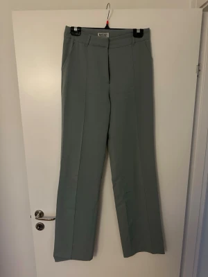 Ljusgröna kostymbyxor från Madlady - Snygga ljusgröna kostymbyxor från Madlady i rak modell med pressveck. Byxorna har hög midja, bälteshällor och diskreta fickor. Perfekta för en clean och stilren look.