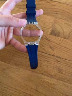 Blå klocka med transparent boett - Säljer ety blått armband och transparent fyrkantig boett. Armbandet har en modern och minimalistisk design med plastmaterial i både armband och boett. Perfekt för dig som gillar en clean och enkel look.