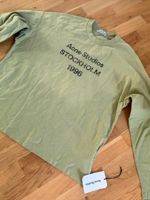 Grön långärmad topp Acne Studios - Cool långärmad topp från Acne Studios i en ljusgrön nyans med tryck 'Acne Studios STOCKHOLM 1996' på bröstet. Tillverkad i mjuk bomull och har en klassisk rund hals. Perfekt för en avslappnad och trendig look.