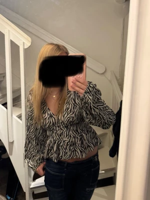 Zebramönstrad blus med v-ringning - Snygg zebramönstrad blus med v-ringning och långa puffiga ärmar. Blusen har en markerad midja och knappar framtill. Tillverkad i ett lätt och luftigt tyg som ger en avslappnad men trendig look.