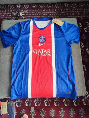 PSG matchtröja blå/röd Nike - Säljer en officiell Paris Saint-Germain matchtröja från Nike i blått och rött med vita detaljer. Tröjan har PSG-logga, Qatar Airways-tryck och klassisk V-ringning. Perfekt för fotbollsfans som vill stötta sitt lag med stil. Storlek M men passar till S