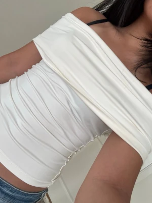 Vit offshoulder topp - Snygg vit offshoulder topp med tight passform och stilren design. Toppen är ärmlös och har en bred omlottkrage som ger en trendig look. Perfekt att matcha med jeans eller kjol för en cool outfit.
