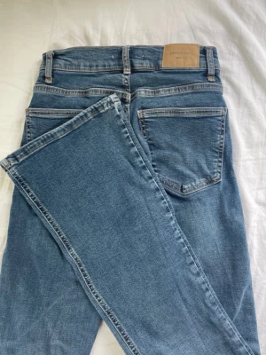 Blå bootcut jeans  - Säljer ett par klassiska blå jeans från Gina tricot bootcut modell. Jeansen har fem fickor, silverfärgade knappar och nitar samt en snygg tvättad finish. Perfekta till en avslappnad look och passar till det mesta i garderoben.
