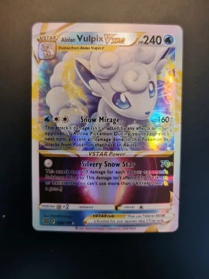 Pokémonkort Alolan Vulpix VSTAR - Säljer ett Pokémonkort med Alolan Vulpix VSTAR-motiv. Kortet har en holografisk yta med färger i blått, vitt och silver. Det är en officiell samlarkort från Pokémon TCG och har coola attacker som Snow Mirage och Silvery Snow Star.